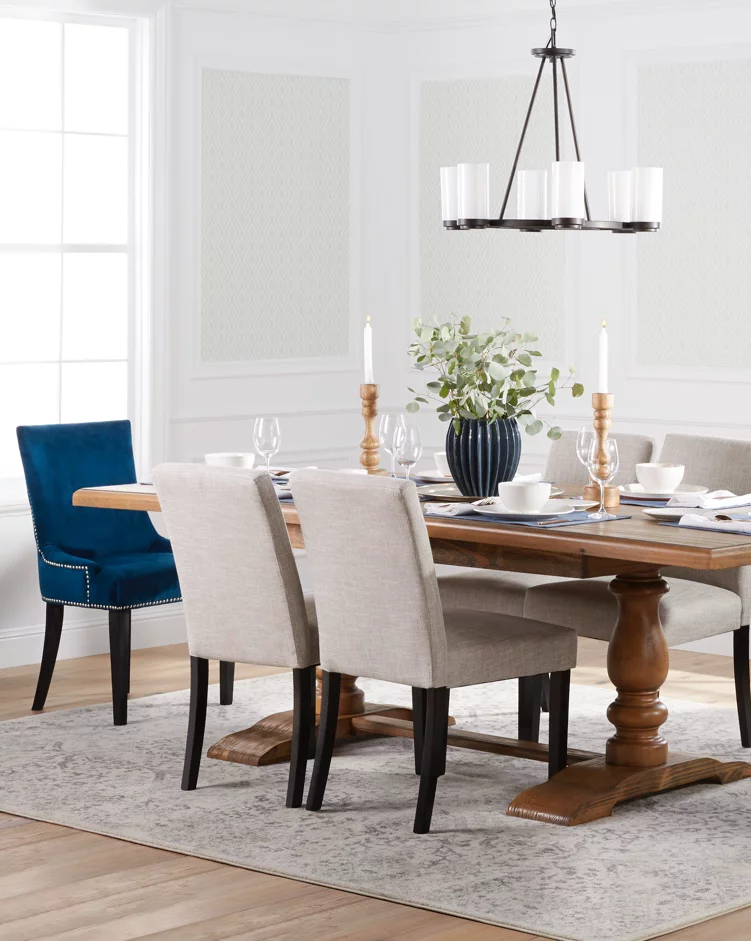 A transitional dining room with a beautiful wooden trestle table, upholstered seating, blue velvet end chairs, an industrial chandelier and a dining table area rug. Links to DX Daily Store's dining room furniture and decor